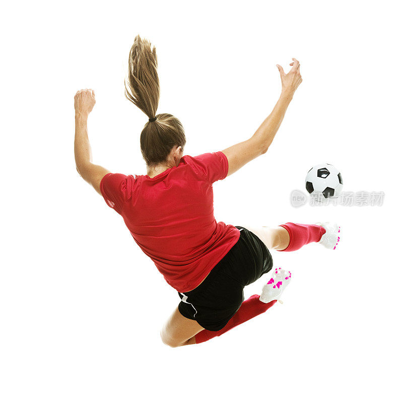全长/后视图/ 20-29岁的成年人漂亮的棕色头发/长发高加索女性/年轻女子足球运动员/运动员/女子足球跳跃/踢/在白色背景前的空中穿着足球制服/运动
